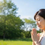 自然の空の下で樹木葬に手をあわせて供養するイメージ画像